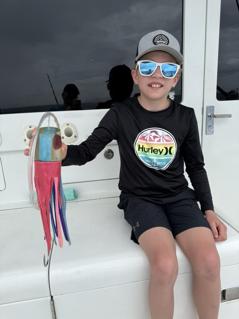 Young angler on a Maui charter boat holding a colorful trolling lure