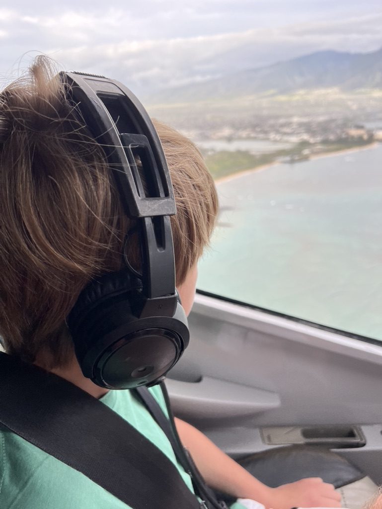 Young guest wearing a headset on a Maui helicopter tour, looking down at the coastline below